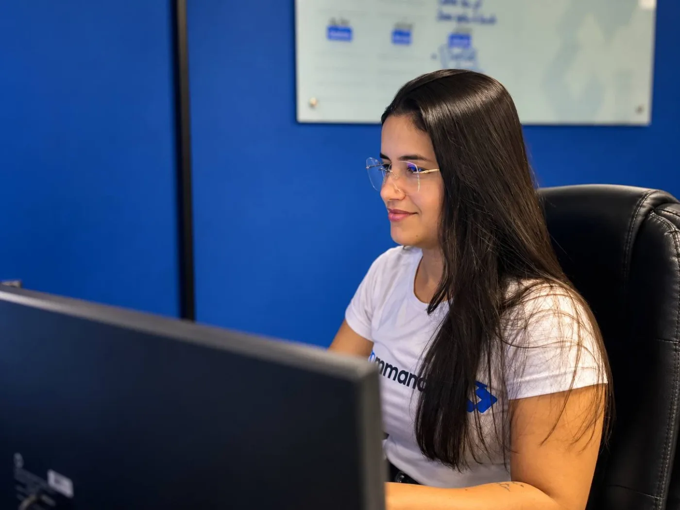 Colaboradora da Command System trabalhando em frente ao monitor, com a parede azul da marca ao fundo